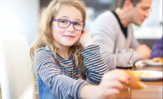 girl wearigng glasses looks at camera as she enjoys a meal with the family
